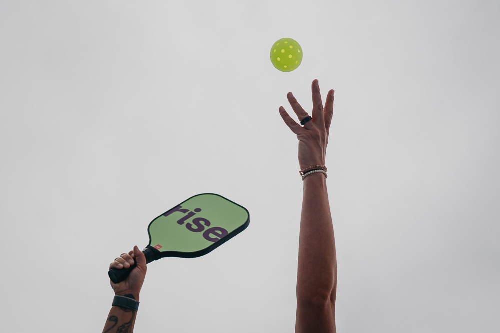 Brand photo of queer woman throwing pickleball.