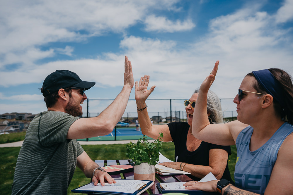 Brand photo of group high-fiving at pickleball court bench.