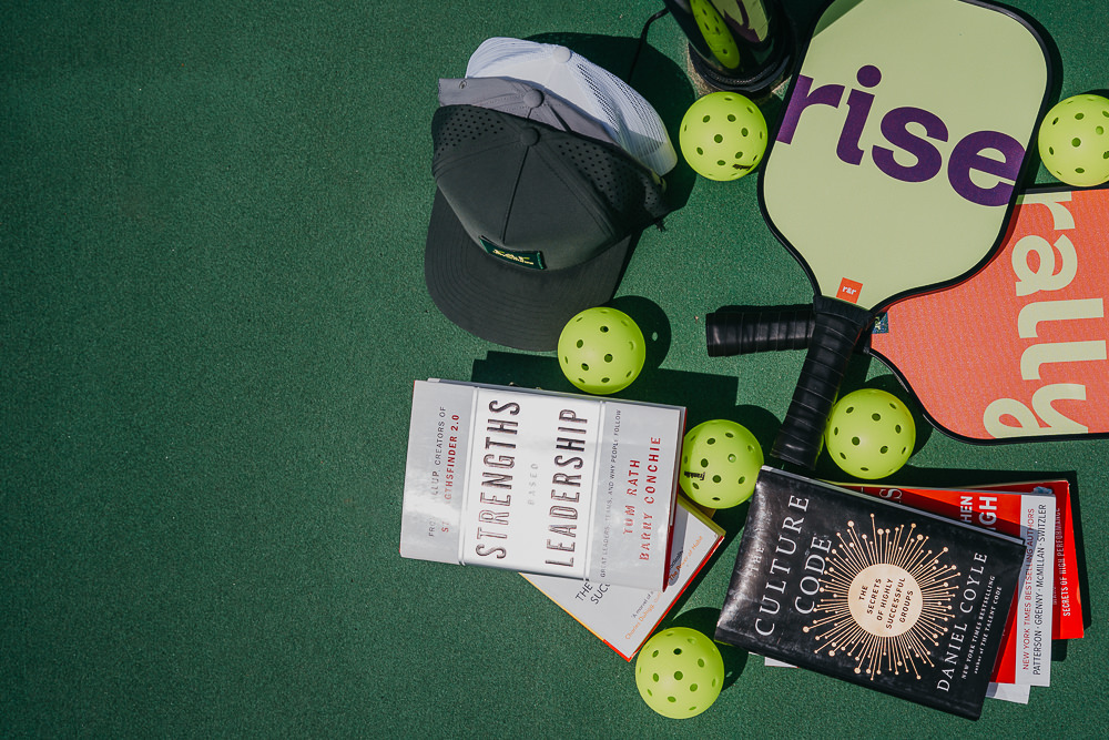 Brand photo of branded hats and paddles on pickleball court.