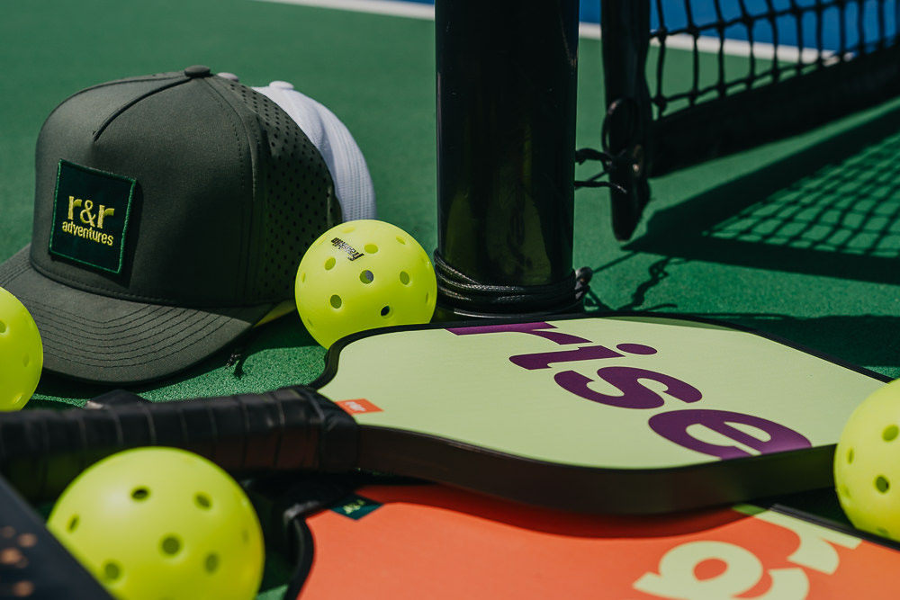 Brand photo of branded hats and paddles on pickleball court.