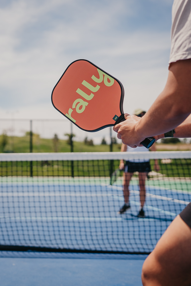 Brand photo of branded Rally paddle on pickleball court.