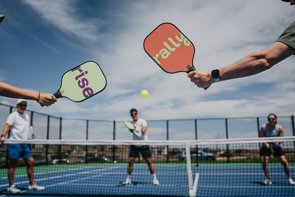 Brand photo of branded rise and rally paddles on pickleball court.