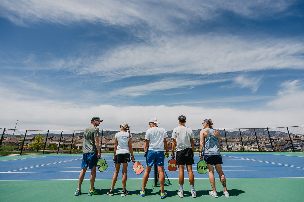 Brand photo of group meeting on pickleball court with mountains in the background.