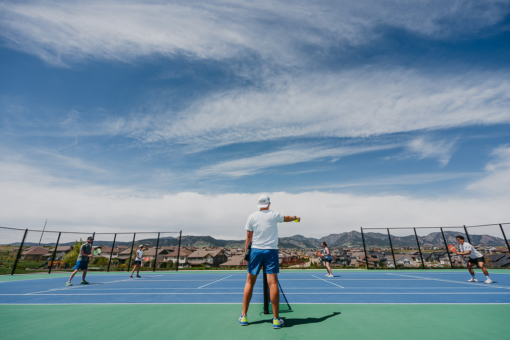 Brand photo of coach pointing to players on pickleball court with mountains in the background.